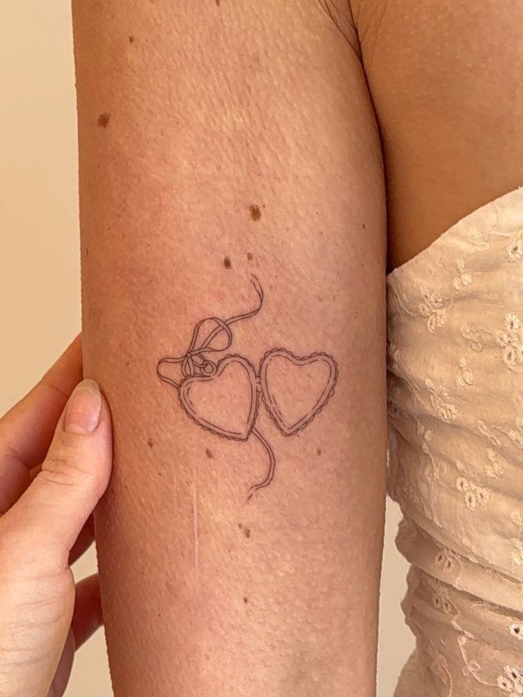 Heart pendant tattoo in fine line style located on the the inner arm.