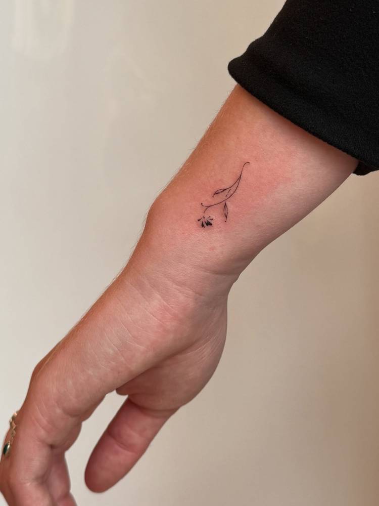 Minimalistic style flower tattoo located on the wrist.