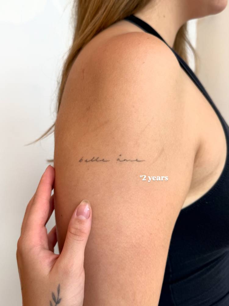 Healed "belle ame" lettering tattoo located on the upper arm.