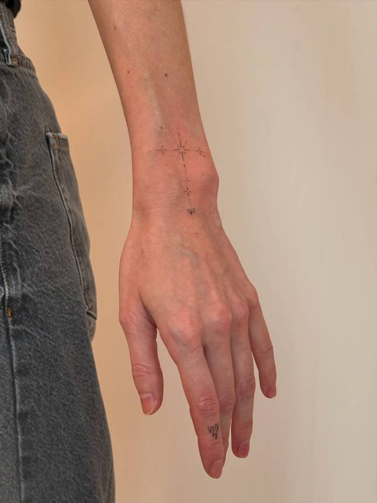 Tiny ornament tattoo in fine line style located on the wrist.