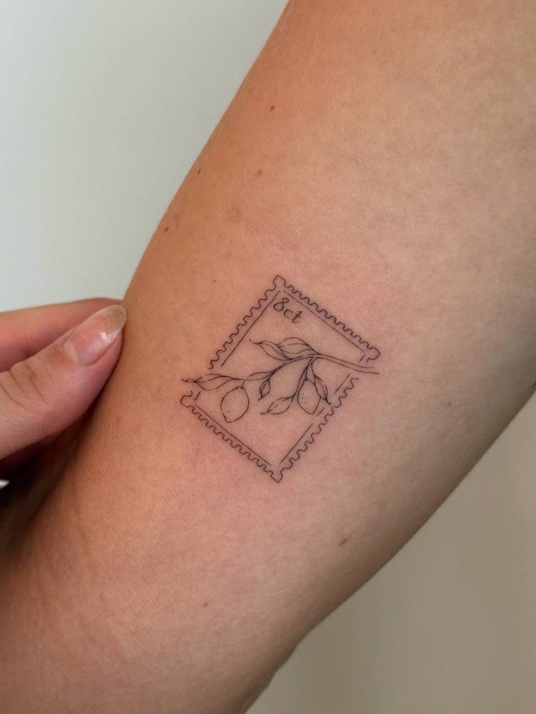Lemon stamp tattoo in fine line style placed on the inner arm.