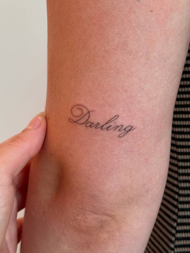 Lettering tattoo of the word "darling" located on the tricep.