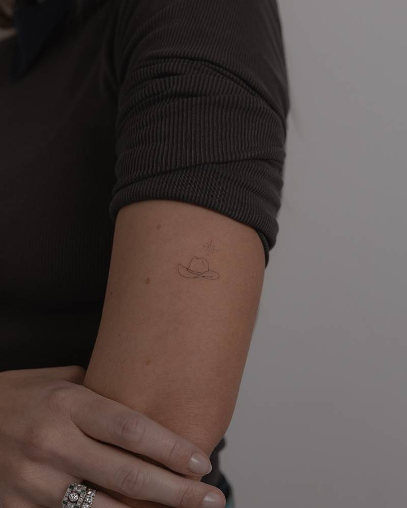 Cowboy hat tattoo in fine line style placed on the upper arm.