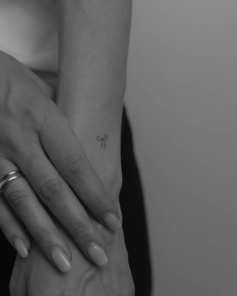 Tiny minimalistic bow tattoo located on the wrist.