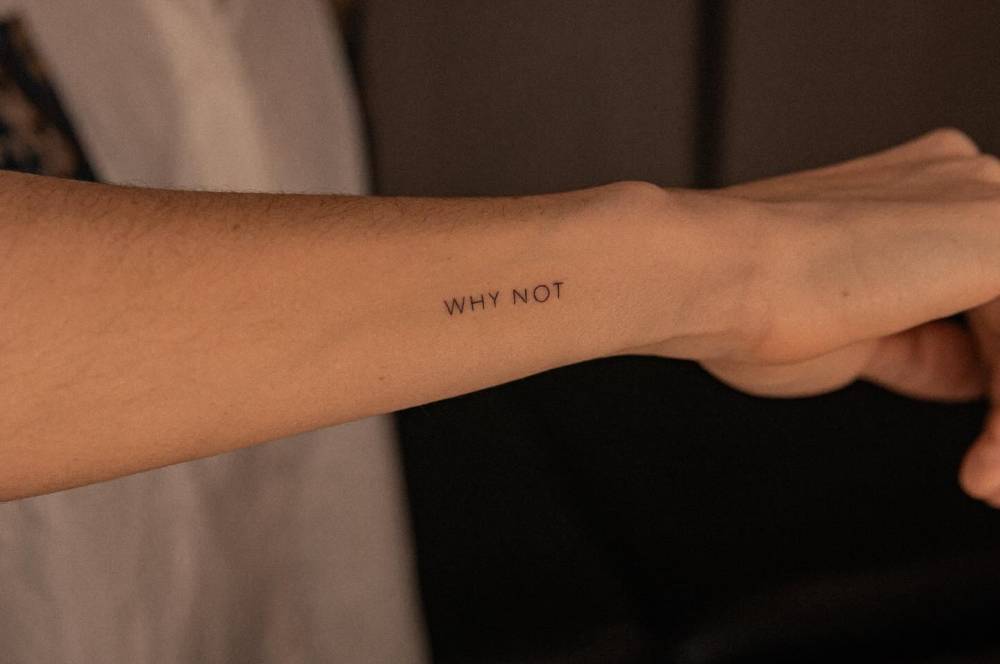 Lettering tattoo that says "why not" located on the wrist.