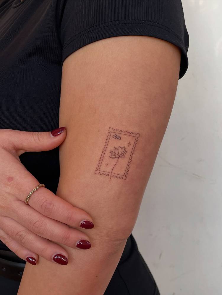 Lotus stamp tattoo in fine line style located on the upper arm.