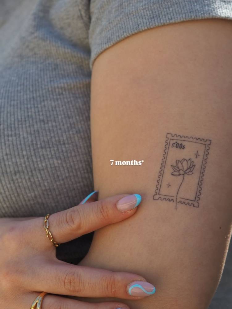 Healed lotus stamp tattoo in fine line style located on the upper arm.