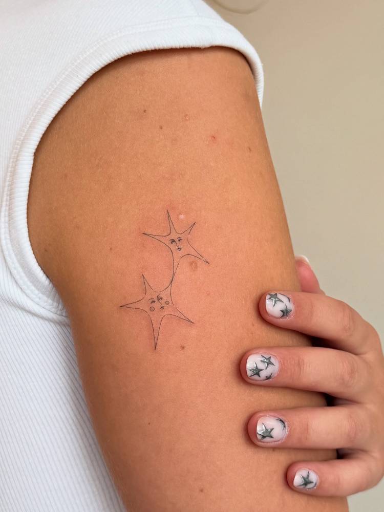 Star couple tattoo in fine line style located on the upper arm.