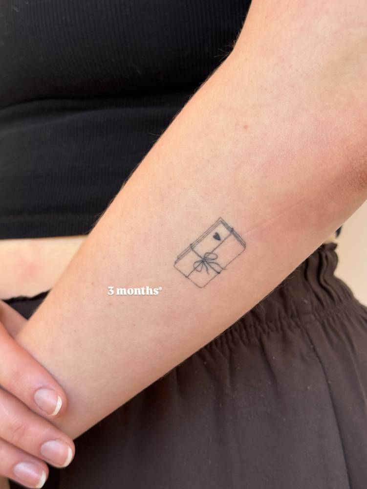 Healed love letter tattoo in fine line style placed on the forearm.
