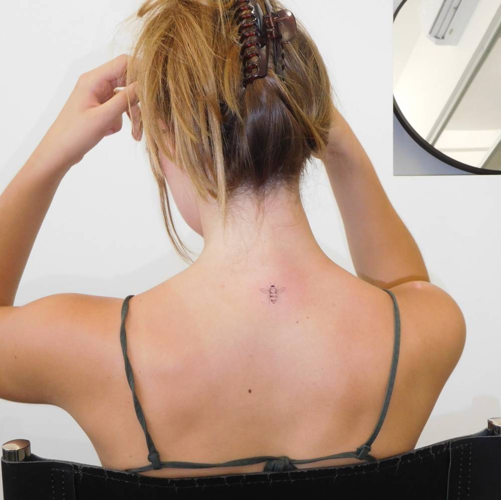 Fine line style bee tattoo located on the upper back.