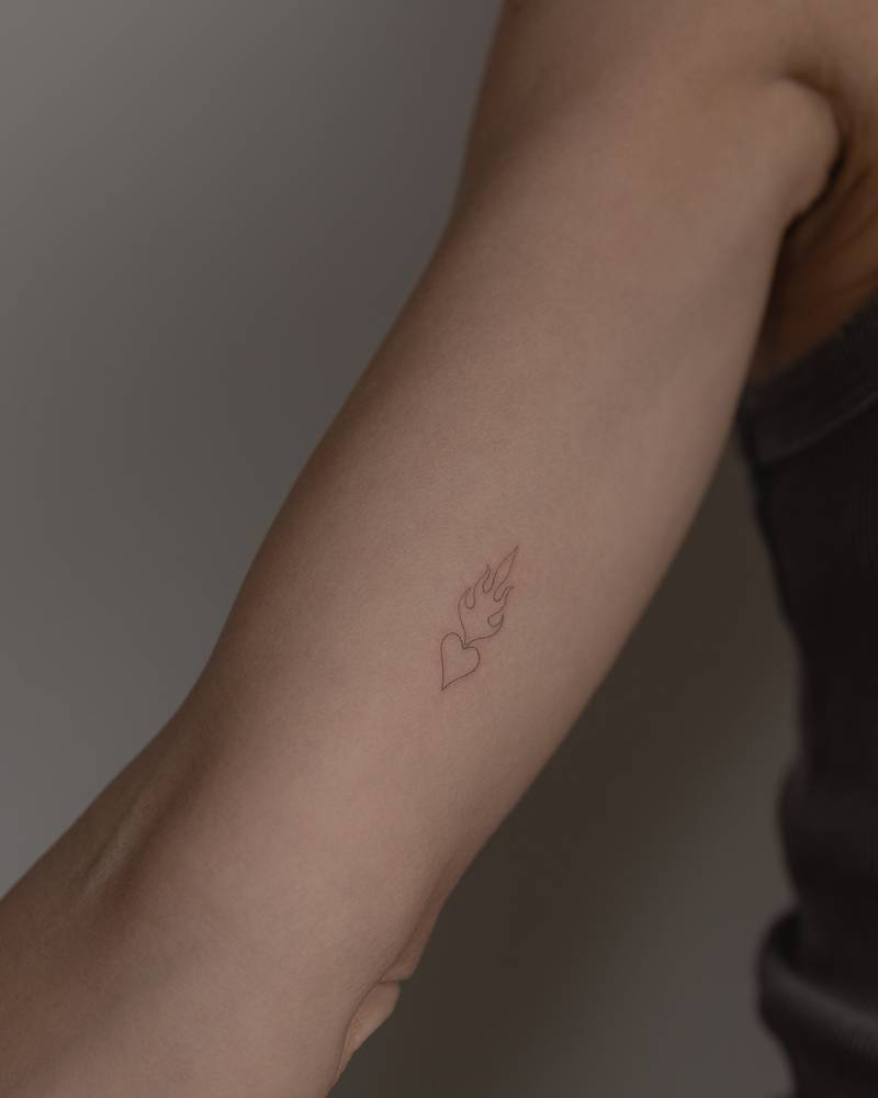 Single needle flaming heart tattoo located on the inner arm.