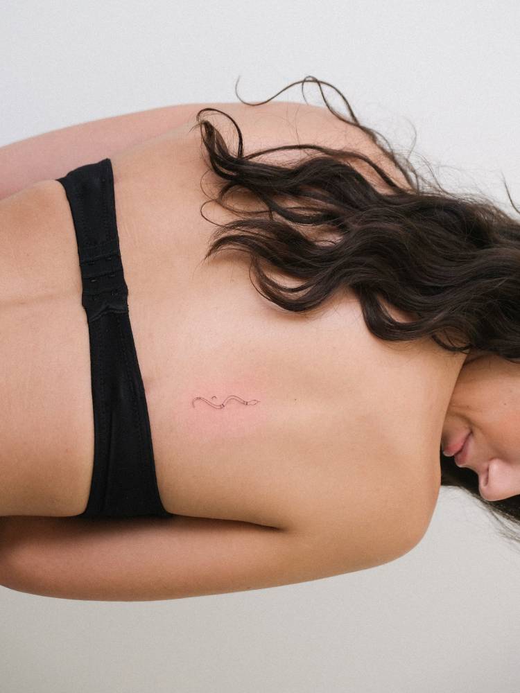 Little snake tattoo in fine line style located on the back.