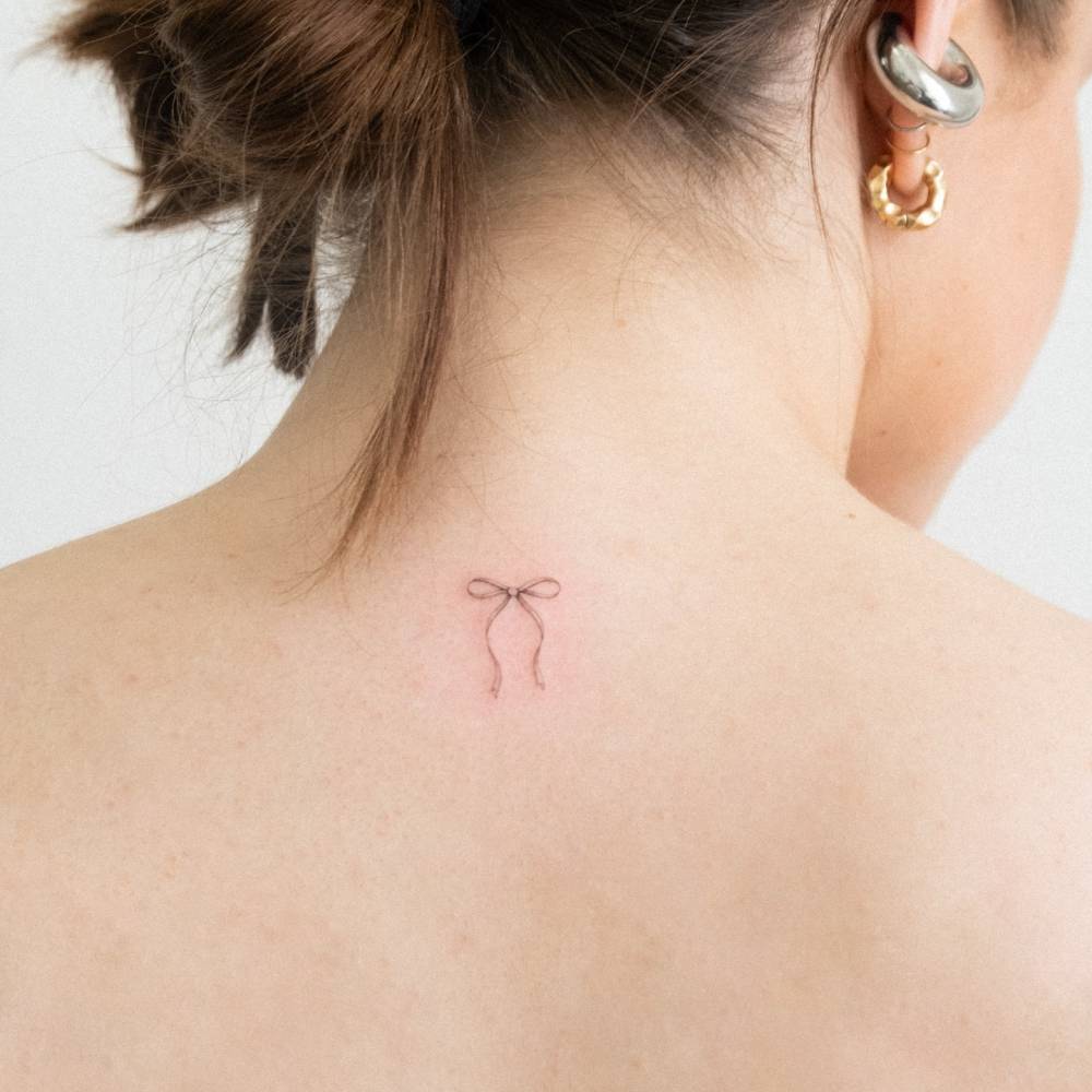 Bow tattoo in fine line style placed on the upper back.