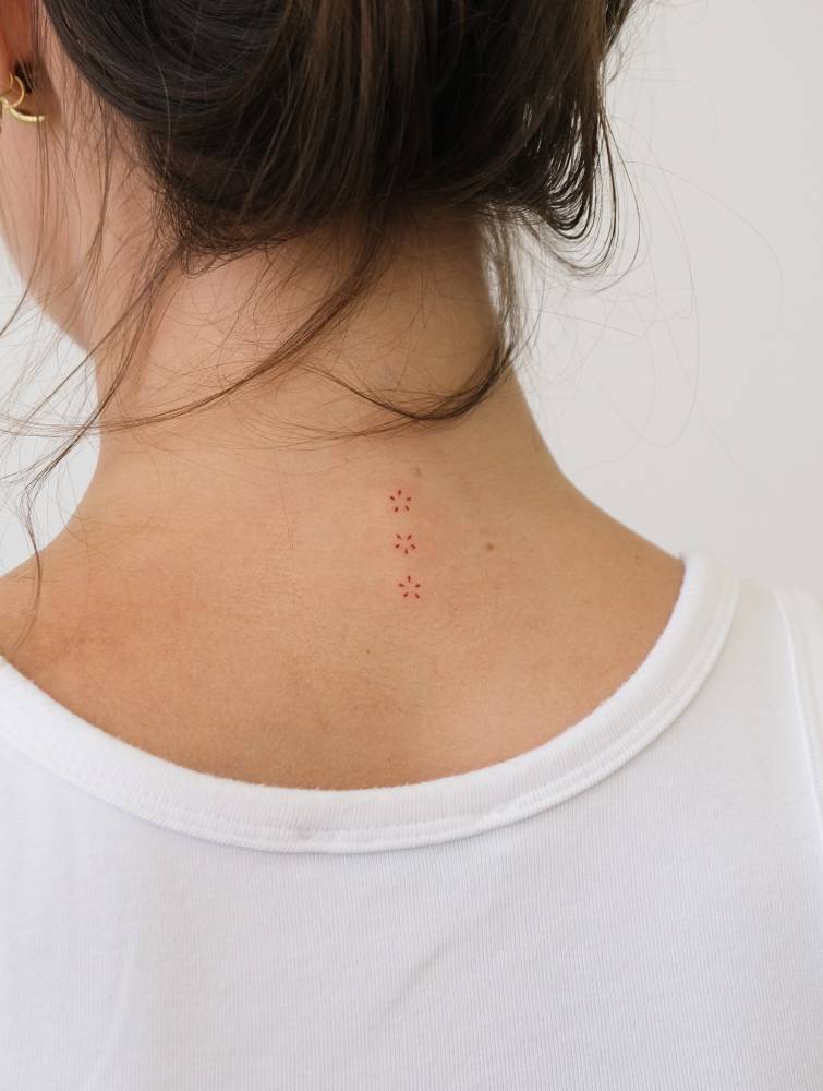 Tiny ornamental red flowers tattoo in minimalistic style located on the upper back.