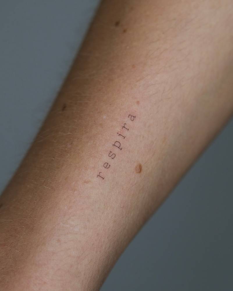 Word "respira" in typewriter font tattooed on the wrist.