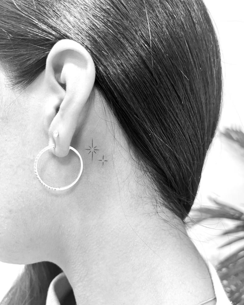 Sparkling stars tattoo in minimalistic style located behind the ear.