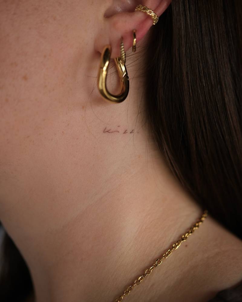 Tiny word "kiss" in handwritten font tattooed on the neck.