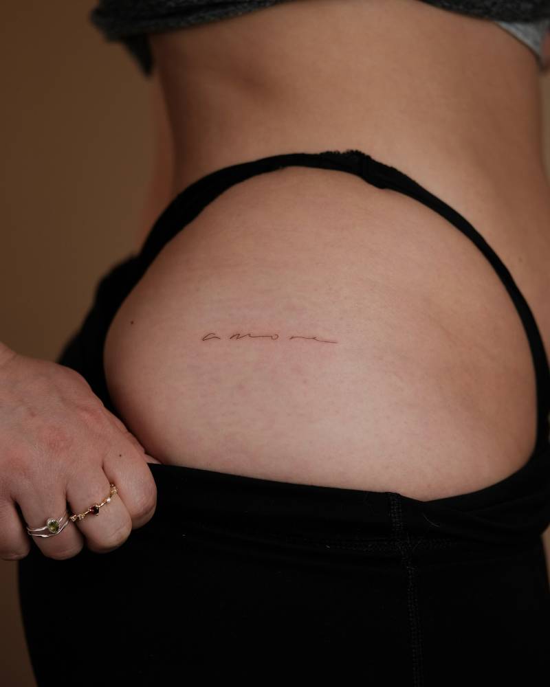 Word "amore" lettering tattoo handwritten on the hip.