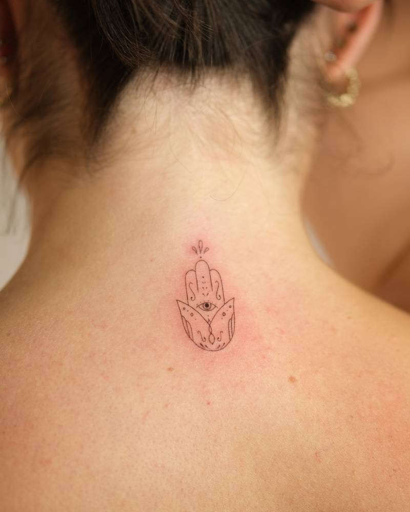 Hamsa tattoo in fine line style located on the upper back.