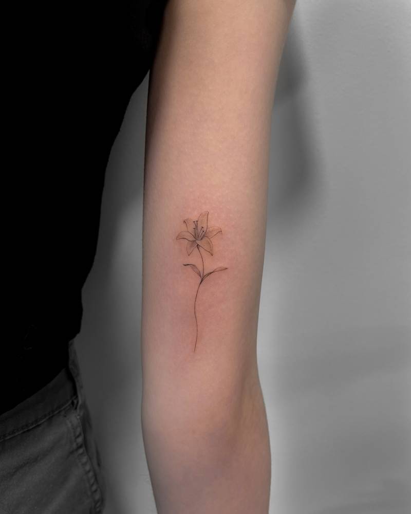 Lily flower tattoo in illustrative style located on the inner arm.
