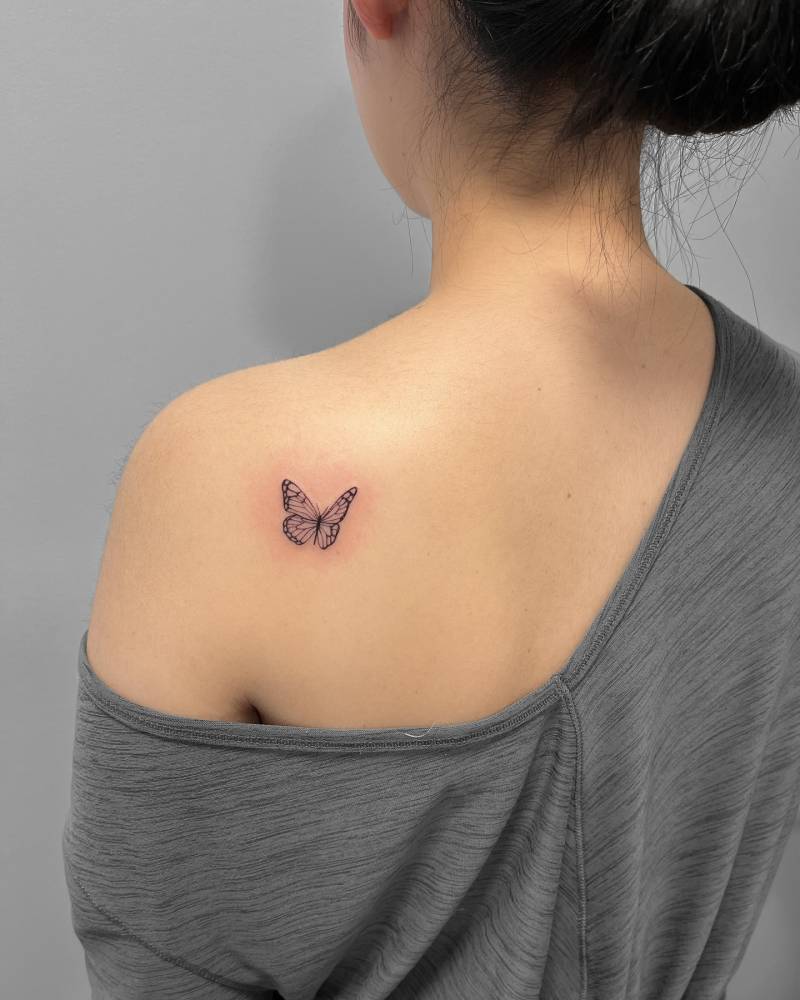 Little butterfly tattoo in fine line style located on the shoulder blade.