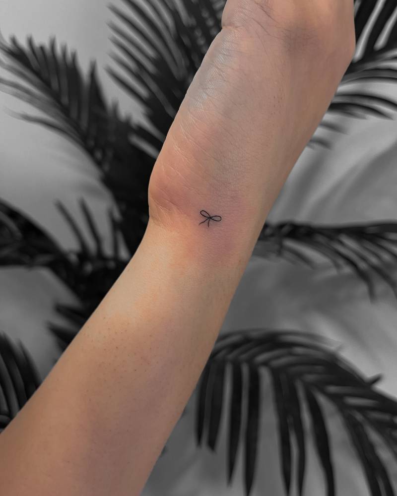 Tiny minimalistic bow tattoo located on the wrist.