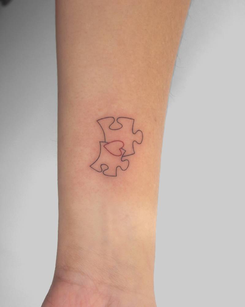 Puzzle pieces and heart tattoo located on the wrist.