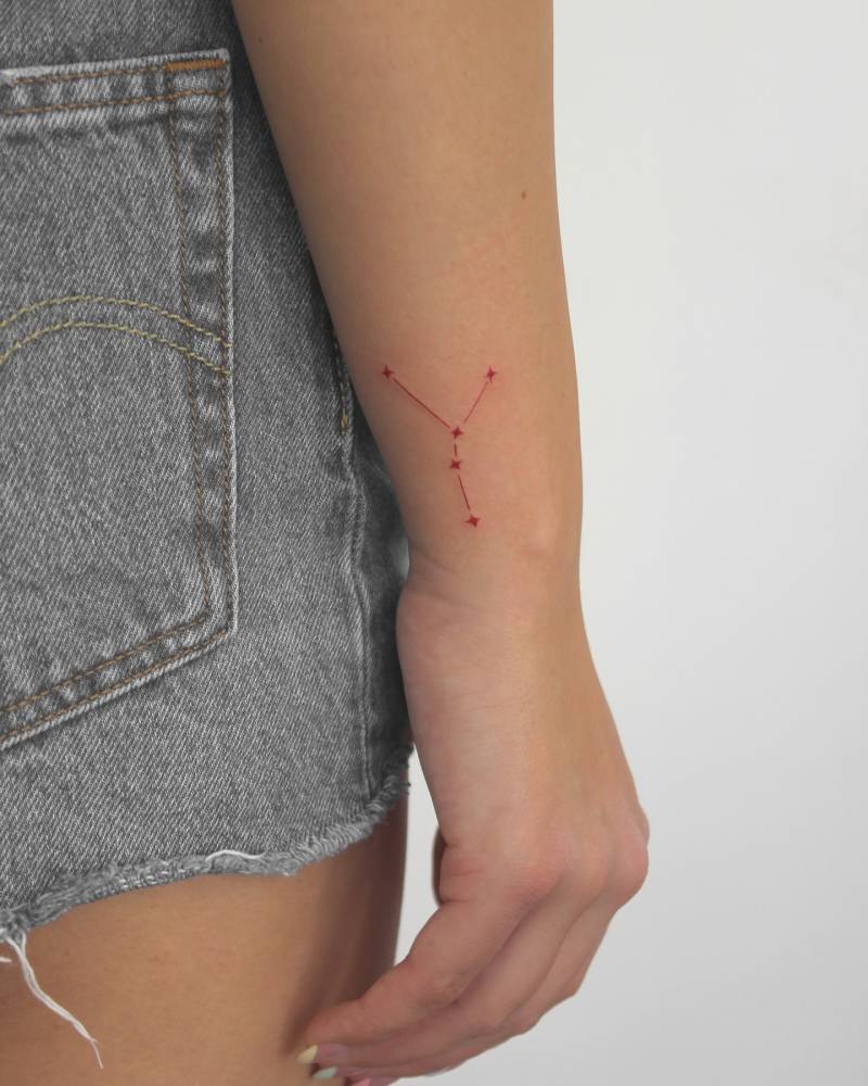 Cancer constellation tattoo in red ink located on the wrist.
