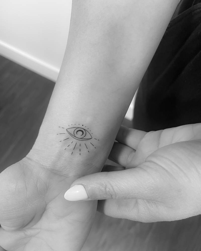 Evil eye tattoo located on the wrist, done in fine line style.