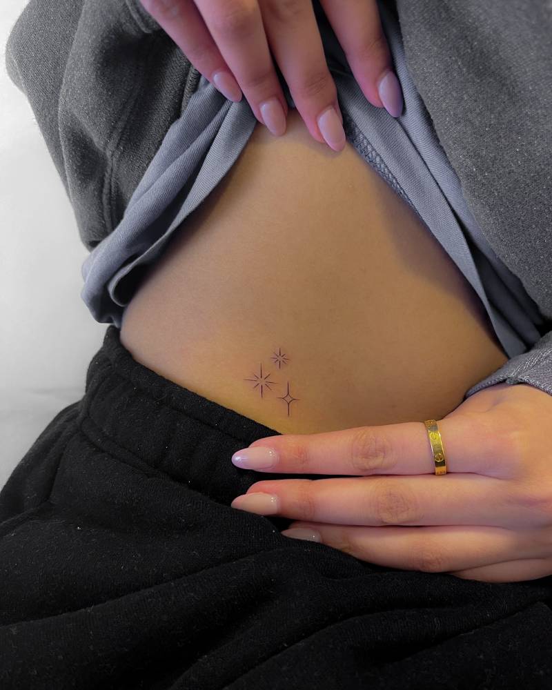 Little sparkling stars tattoo in minimalistic style located on the waist.