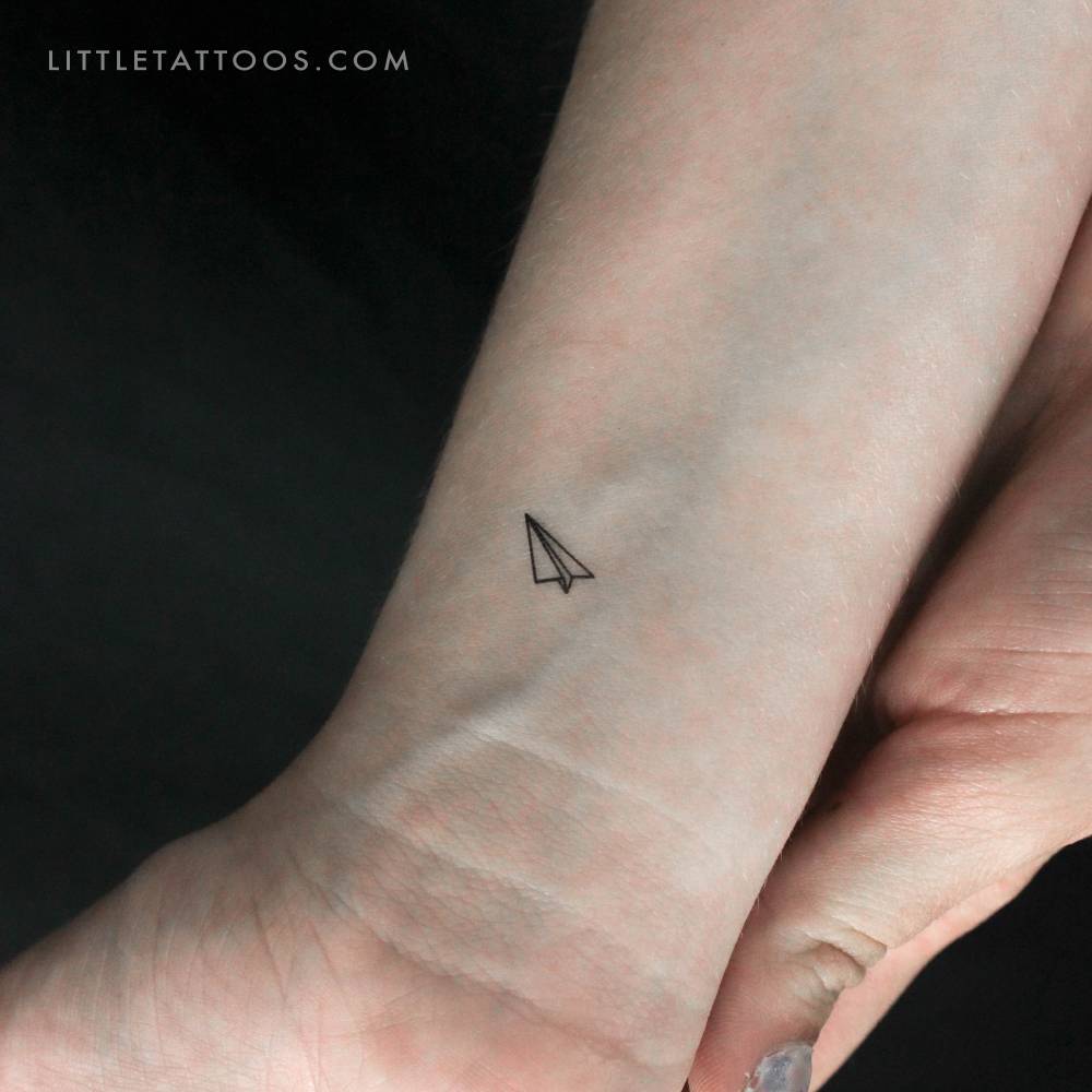 Tiny minimalistic paper plane temporary tattoo located on the wrist.