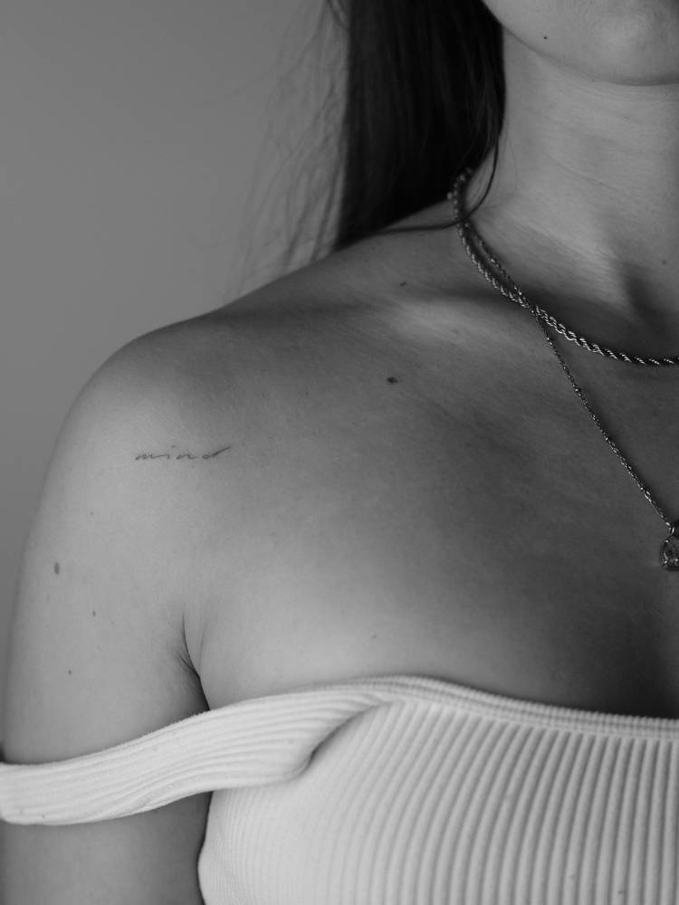 Tiny lettering tattoo of the word "mind" located on the shoulder.