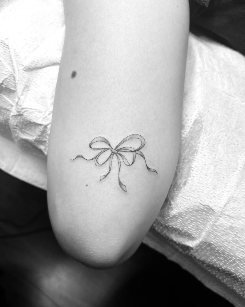 Illustrative style bow tattoo placed on the tricep.