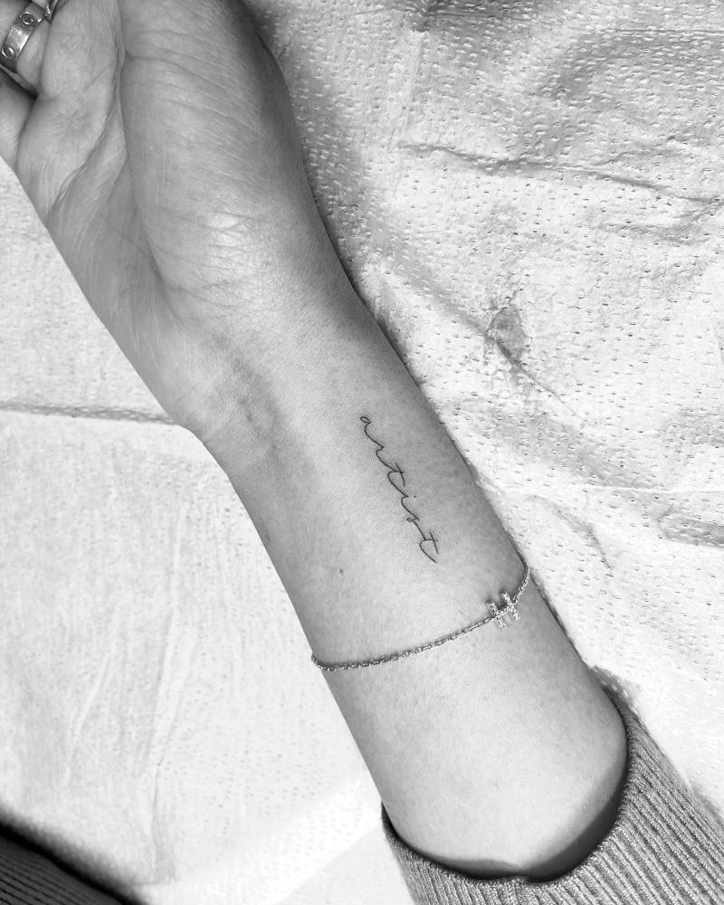 Word "artist" in handwritten font tattooed on the wrist.