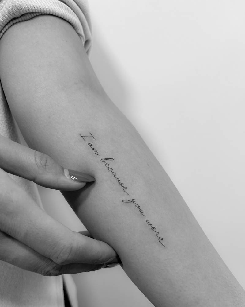 "I am because you were" lettering tattoo handwritten on the inner forearm.