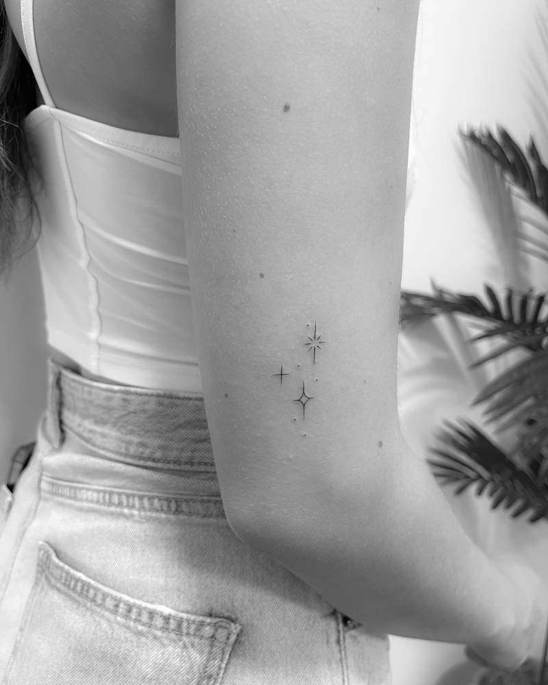 Sparkling stars tattoo in minimalistic style placed on the upper arm.