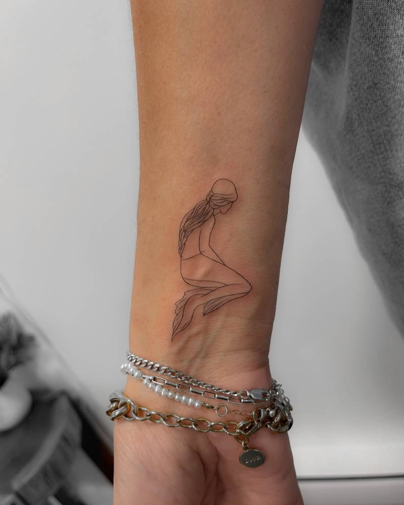 Fine line mermaid tattoo located on the wrist.