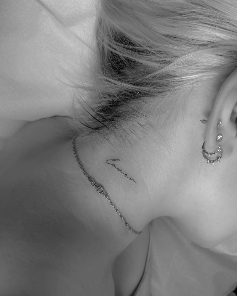 Handwritten font word "lover" tattooed on the neck.
