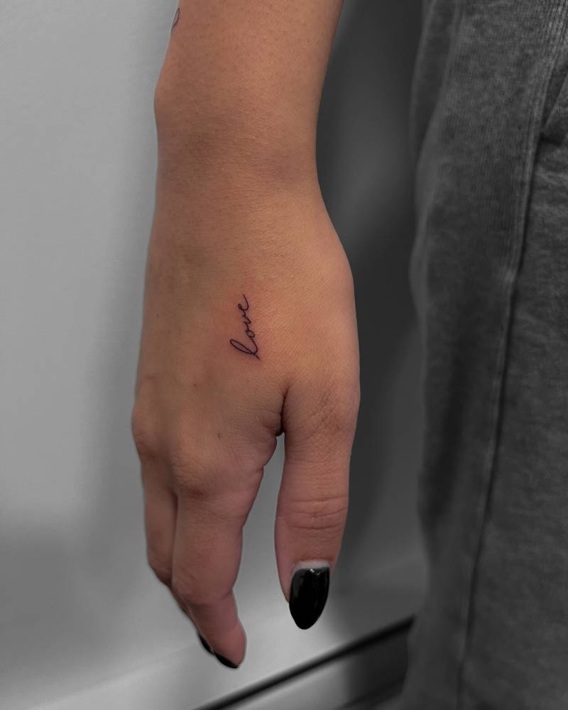Tiny word "love" lettering tattoo placed on the hand.