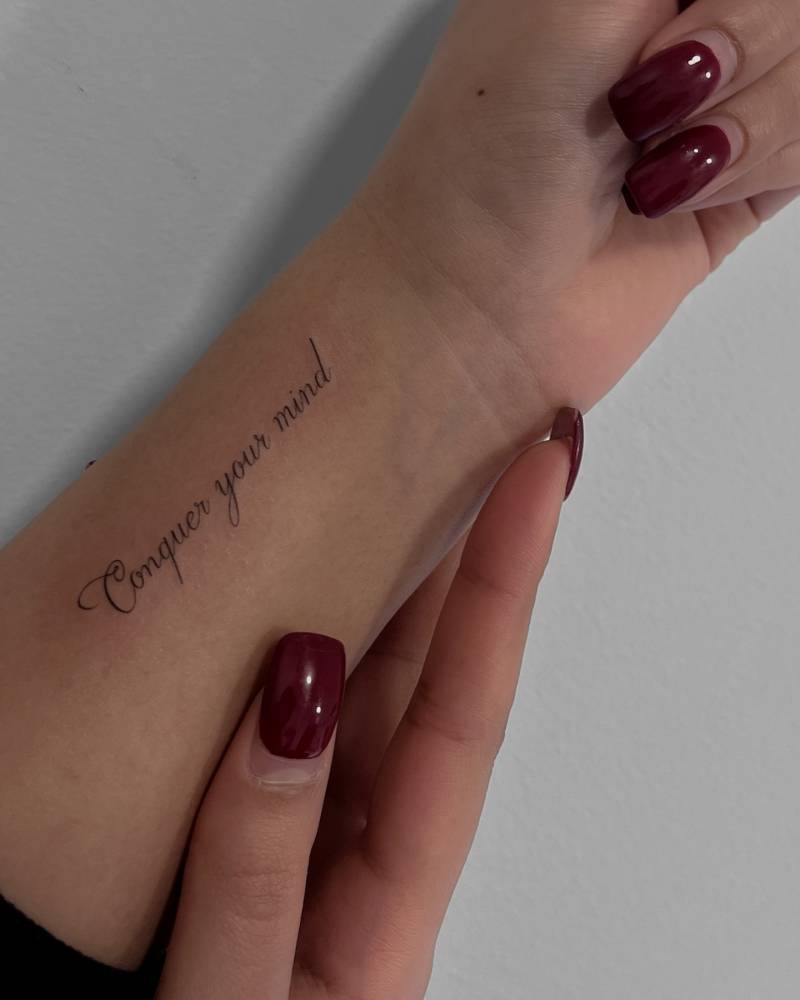 "Conquer your mind" lettering tattoo placed on the wrist.
