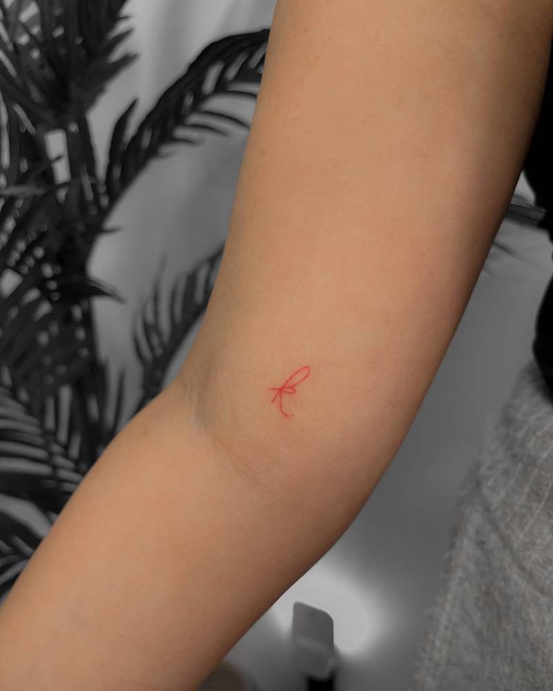 Tiny letter "K" tattoo in red ink placed on the inner arm.