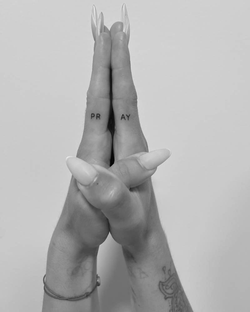 Individual matching tattoo of the word "pray" located on the fingers.