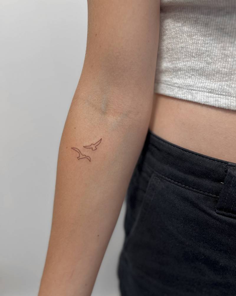 Flying birds tattoo in fine line style placed on the inner forearm.