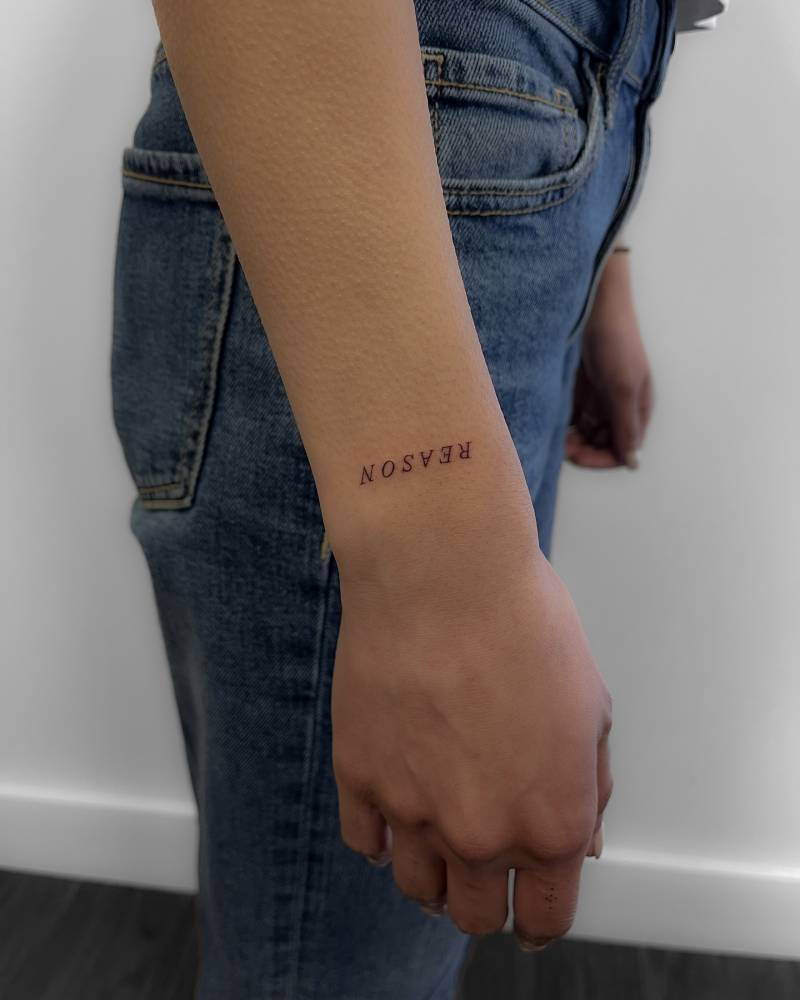 Lettering tattoo of the word "reason" located on the wrist.