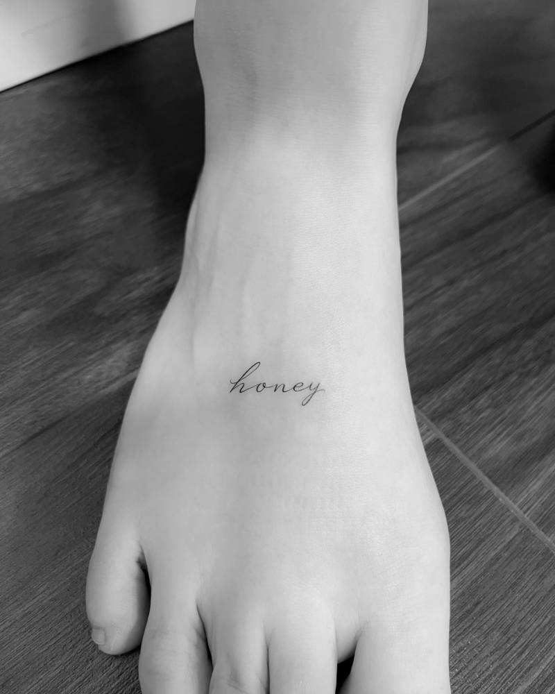 Lettering tattoo of the word "honey" located on the foot.