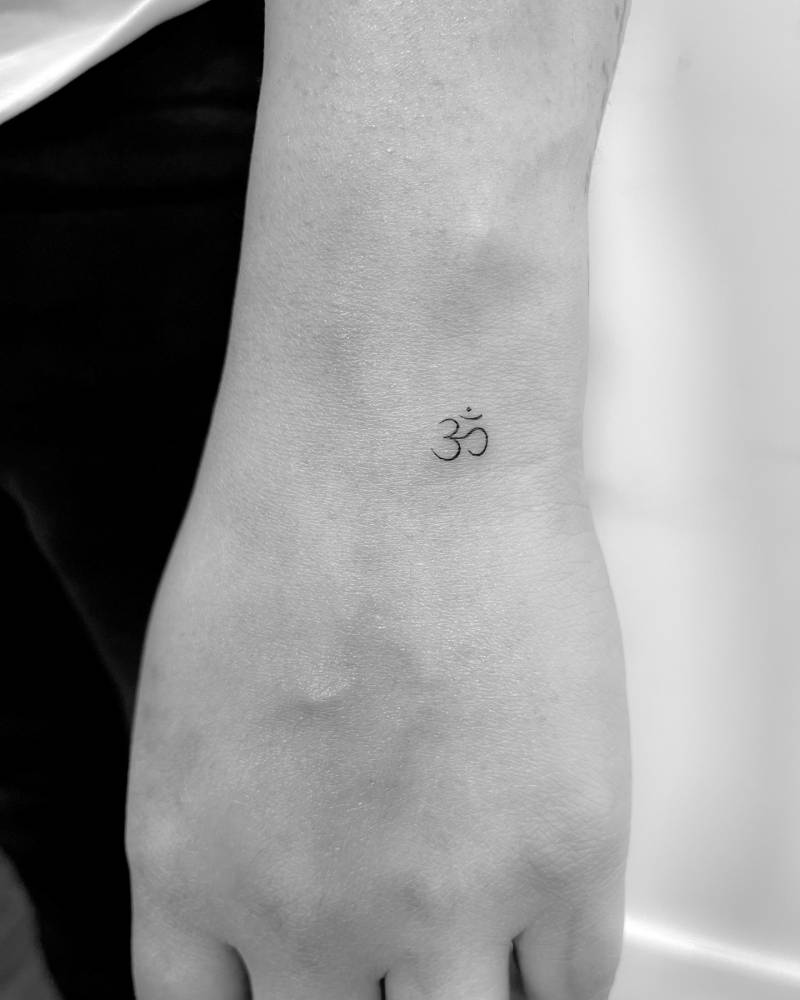 Tiny Om tattoo in minimalistic style placed on the wrist.