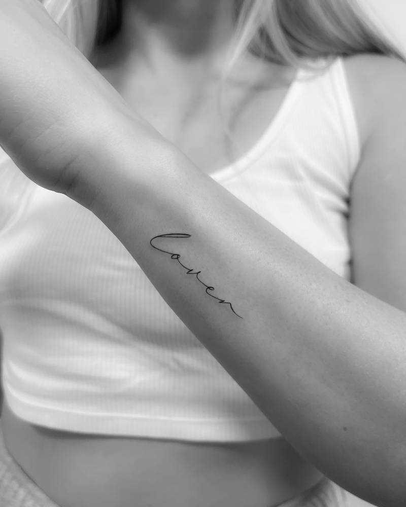 Word "lover" tattoo located on the wrist.