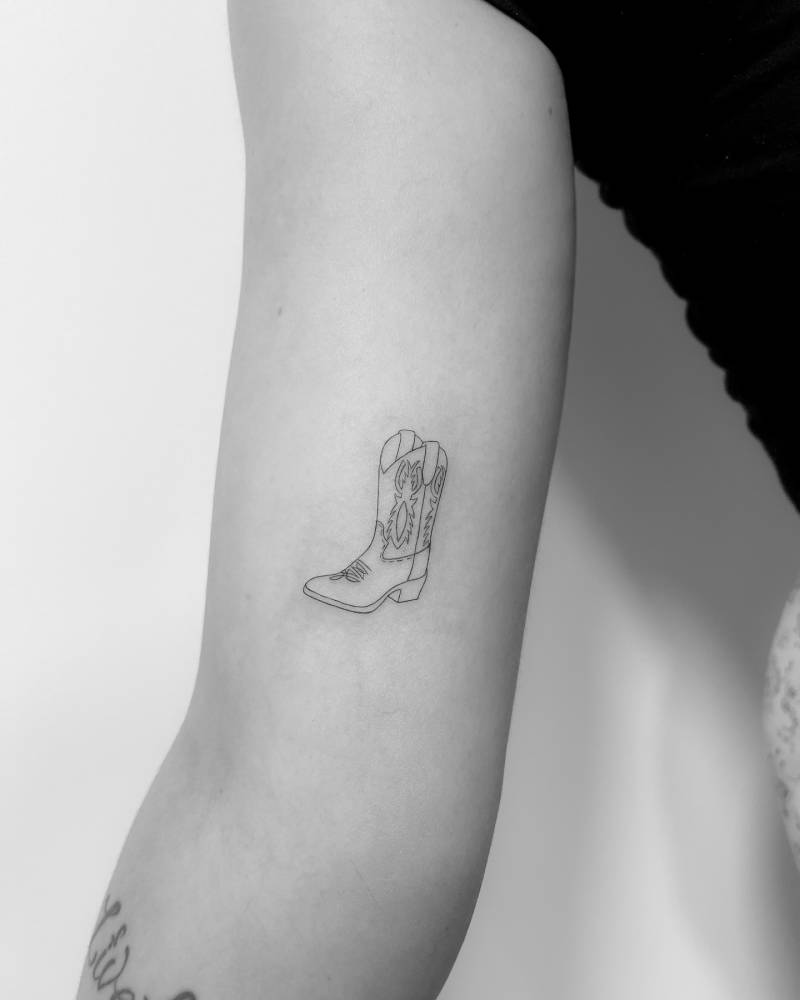 Cowboy boot tattoo placed on the inner arm, done in fine line style.