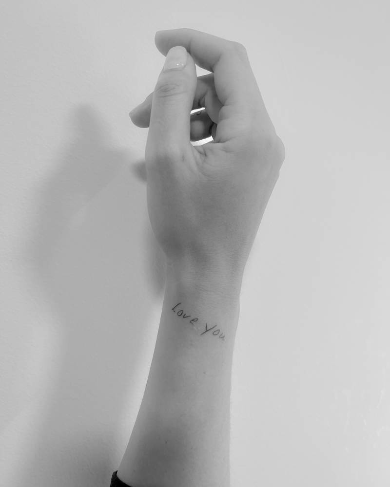 Handwritten font lettering tattoo that says "love you" located on the wrist.