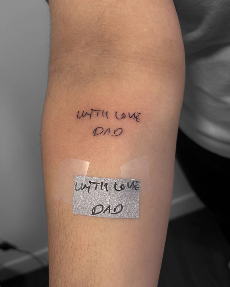 "With love, dad" lettering tattoo in handwritten font done on the inner forearm.